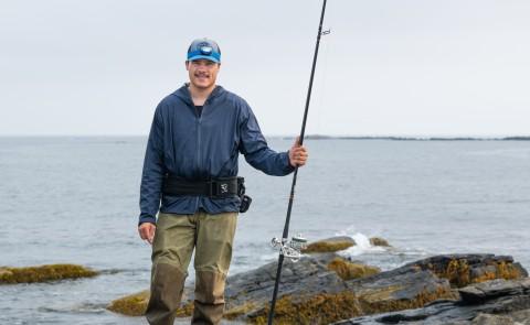 A UNE student poses with a fishing rod in front of the ocean